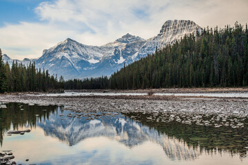 Snow capped peaks reflected in the Athabasca River  in the Canadian Rockies, viewed from the Icefields Parkway, which extends from Banff to Jasper, Alberta, Canada.