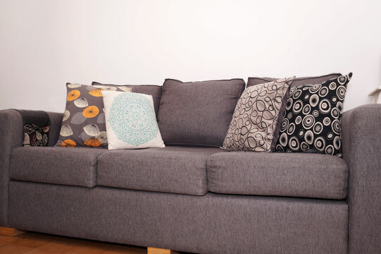 Close Up View Of Large Grey Couch Middle Area With Colorful Pillows On Top.  Taken Indoors Under A White Bright Light.