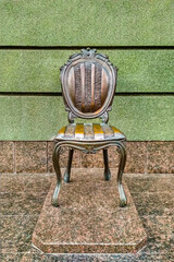 Bronze chair monument on a marble pedestal against the background at the green wall