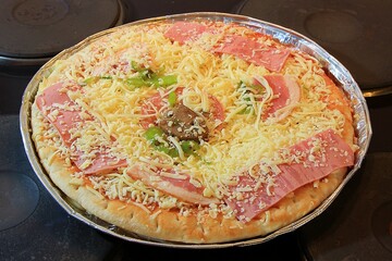 Frozen special pizza in an aluminum tray on a cooktop ready to bake in the oven. Shallow depth of field