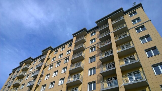 Facade Of New Multi-story Residential Building. Sale And Rental Apartments. Housing Affordability And Development. Cityscape. City Living. Real Estate Investing. Mortgage Concept. Blue Sky Background.