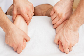Fototapeta na wymiar Hands of two massagers are giving massage to soft bare feet during spa foot treatment.