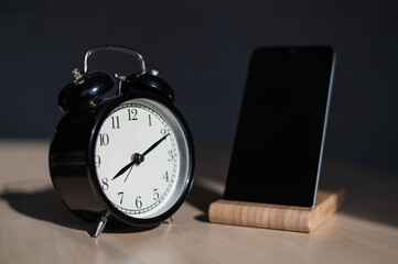 Classic alarm clock and smartphone on a stand on a wooden table. No people.