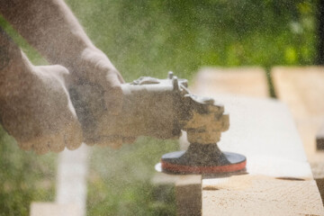 Carpenter at work sanding the wood with sanding machine blurry background. Young men with carpenter tools outdoor blurry.