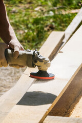 Carpenter at work sanding the wood with sanding machine. Young men with carpenter tools outdoor. Carpenter with polishing machine, grinding the wood. Handyman at work.