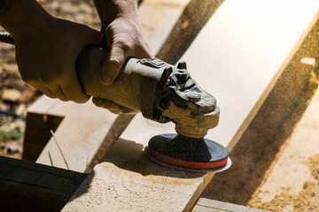 Carpenter at work sanding the wood with sanding machine. Young men with carpenter tools outdoor. Carpenter with polishing machine, grinding the wood. Handyman at work.