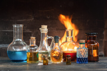 Colorful magic potion bottles on wooden table on burning fire in fireplace background. Witch doctor table.