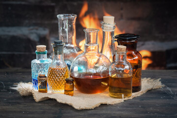 Colorful magic potion bottles on wooden table on burning fire in fireplace background. Witch doctor...
