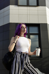 young woman in stylish clothes with a cup of coffee. sunglasses, striped pants and white sneakers. walk in the city. Attractive girl in casual wear