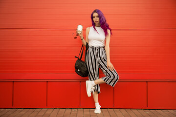 young woman in stylish clothes with a cup of coffee. sunglasses, striped pants and white sneakers....