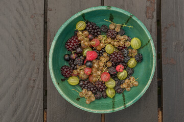 Mixed color garden fruit on wooden brown table and orange and green dish