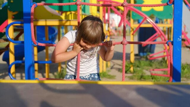Child girl playing and laughing on the playground, riding on the carousel, climbing the wall.