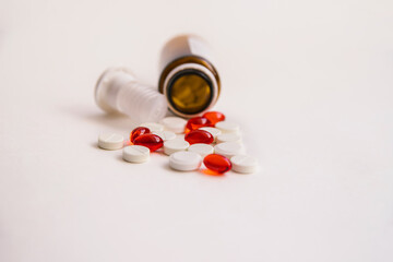 Tablets and capsules are scattered from a bottle of dark color on a white background.Medicines and pharmacy.