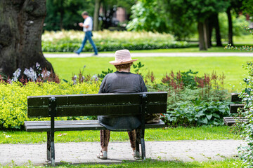 An old woman rests in a park bench on a hot summer day