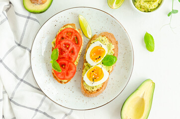 Toasts with mashed avocado, boiled eggs, fresh tomato and basil on a white concrete background. Healthy food. Horizontal, copy space.