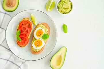Fototapeta na wymiar Toasts with mashed avocado, boiled eggs, fresh tomato and basil on a white concrete background. Healthy food. Horizontal, copy space.