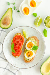 Toasts with mashed avocado, boiled eggs, fresh tomato and basil on a white concrete background. Healthy food. Vertical, copy space.