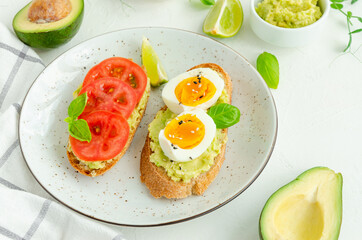 Toasts with mashed avocado, boiled eggs, fresh tomato and basil on a white concrete background. Healthy food. Horizontal, copy space.