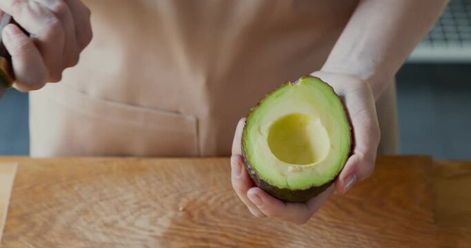 Woman removing avocado seed with knife at kitchen