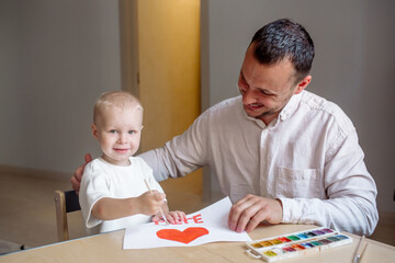 Boy with dad holding a homemade greeting card in his hands with a congratulation to his mother for mother's day in French
