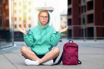 Female student sitting in lotus position and meditating with a stack of books on her head.