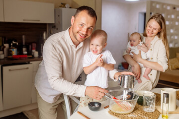 Little boy 2 years old preparing dough with dad, mom and newborn sister in the kitchen at home

