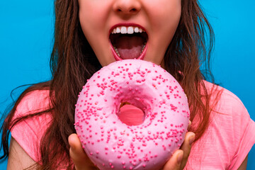 girl bites a pink donut on a blue background. sweets.