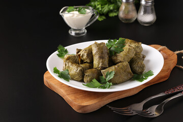 Dolma - stuffed grape leaves with rice and meat on a white plate on wooden board. Traditional Caucasian, Greek, Ottoman and Turkish cuisine, Closeup