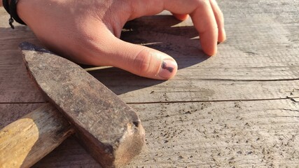 A hammer and a finger with a black bruised nail against the background of an old wooden table. very painfully.