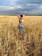 Young happy beautiful slender girl with long black hair and a hat in a wheat field. Summer landscape