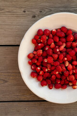 wild strawberries on a white plate on a wooden background