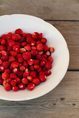 wild strawberries on a white plate on a wooden background