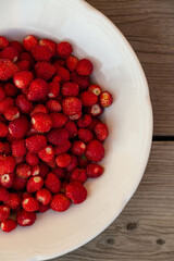 wild strawberries on a white plate on a wooden background