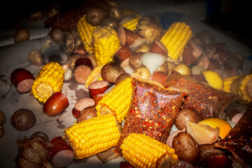 Spice packets along with corn on the cob and sausage and potatoes and onions poured onto brown paper  covered table at shrimp boil