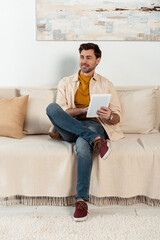 Handsome smiling man using digital tablet on couch at home