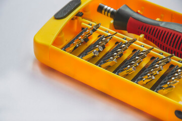 Close up picture of screwdriver with different nozzles for work in yellow box on light background located on left side. Copy space with empty space concept for text. Wallpaper for engineering works.