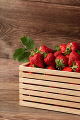 Background from freshly harvested strawberries in wooden box. Wooden clean box with bright, red juicy strawberries. Fresh ripe juice strawberries in box over wooden background. Top view