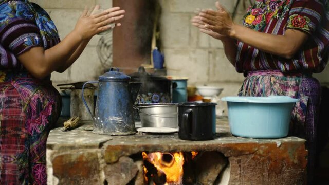 A pair of indigenous women dressed in traditional clothes make tortillas over a firewood kitchen in Guatemala.