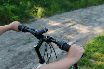 Fototapeta na wymiar close up image of boy's hands hold black handlebar of bike while riding bicycle on countryside road. Happy summer vacation concept.