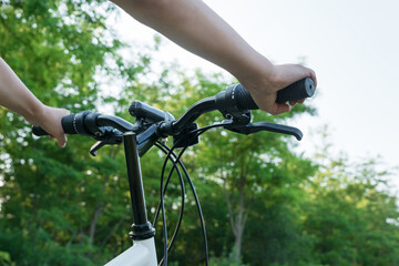 Fototapeta na wymiar child's hands hold black handlebar of bike while riding bicycle on countryside road in green forest. Happy summer vacation concept.