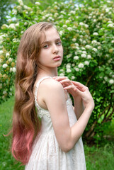  beautiful white girl 11 years old with long hair in a white dress in a blooming garden