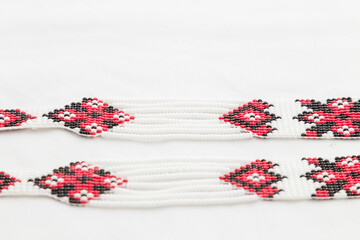 Beaded ethnic red and black necklace on white fabric background. Female accessories, decorative ornaments and jewelry. Fashion and style concept. Soft focused close up shot.