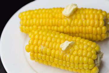 Boiled corn with butter and salt on a white plate on a black background.