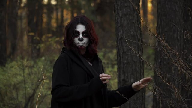 Girl with mystery makeup of a dead man in nature in sun. Theme of costumes and transformation for holiday of Halloween. Traditional skull makeup for the day of the dead Santa Muerte celebration