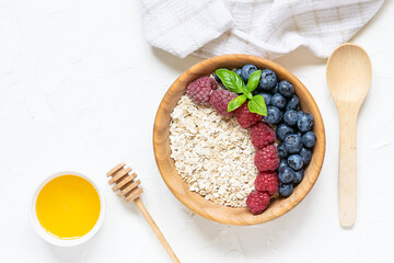 Tasty and healthy breakfast concept. Oat flakes with berries and honey on white concrete background top view. 
