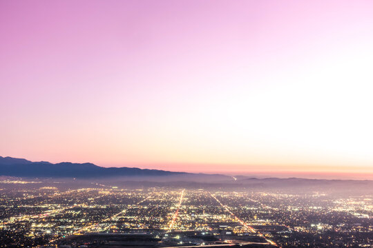 The city lights of the skyline of the Inland Empire near Los Angeles California begin to appear as the sun sets in a dramatic pink sunset. View from Potato Mountain in Claremont Wilderness Park