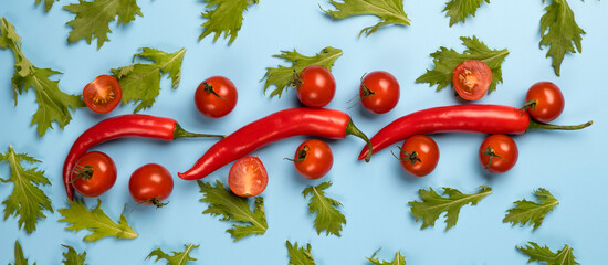 Red chili peppers, tomatoes and green rucola salad leaves on blue background.