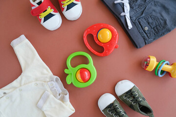 Baby goods on brown background. Clothes, footwear and toys for infant baby boy. Flat lay design.
