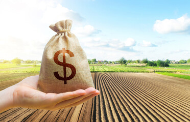 A hand holds out a dollar money bag on a background of a farm field. Lending farmers and...