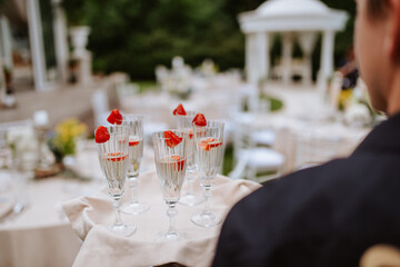 The waiter serves a glass of champagne with strawberries on a tray
